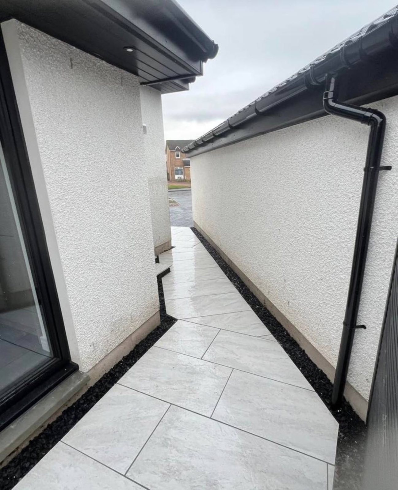 The side return nobody bothers with, done properly — porcelain paving run the full length between two houses with a slate drainage margin either side.