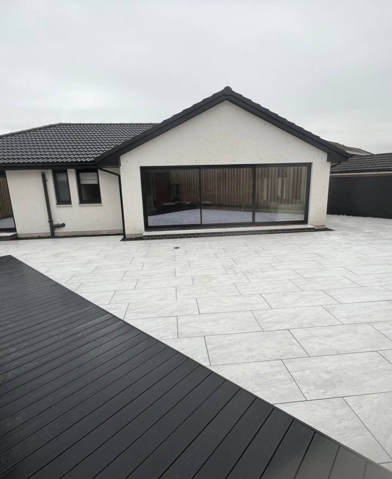 A large marbled porcelain terrace wrapping a rendered bungalow, finished against a run of dark composite decking — two surfaces, one level, no trip.